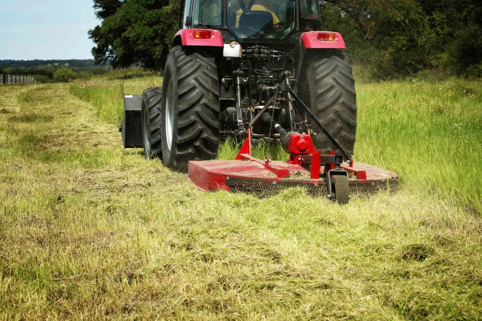 Rotary cutter behind a tractor cutting tall field grass