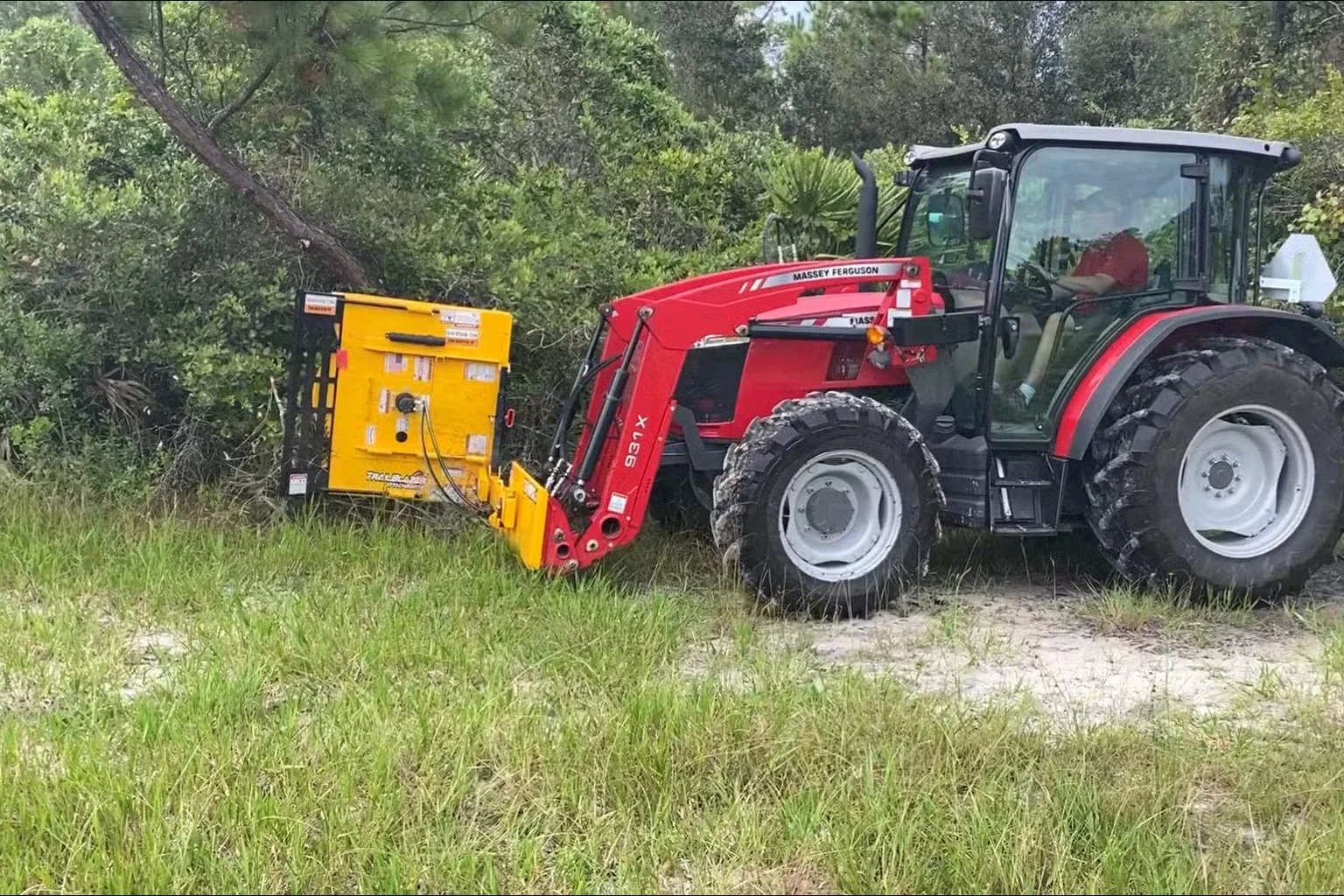 Tractor and brush-cutting equipment beside an overgrown tree line